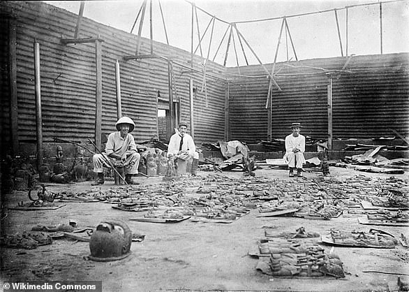 The interior of the Oba's palace after it was burned during the sacking of Benin. Bronze plaques are seen laid out in the foreground as members of the expedition force sit around