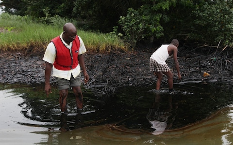 Men walk in an oil slick covering a creek near Bodo City in the oil-rich Niger Delta region of Nigeria