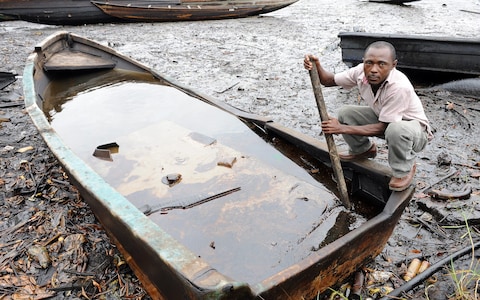An indigene of Bodo, Ogoniland region in Rivers State, tries to separate with a stick the crude oil from water in a boat at the Bodo waterways polluted by oil spills attributed to Shell equipment failure August 11, 2011